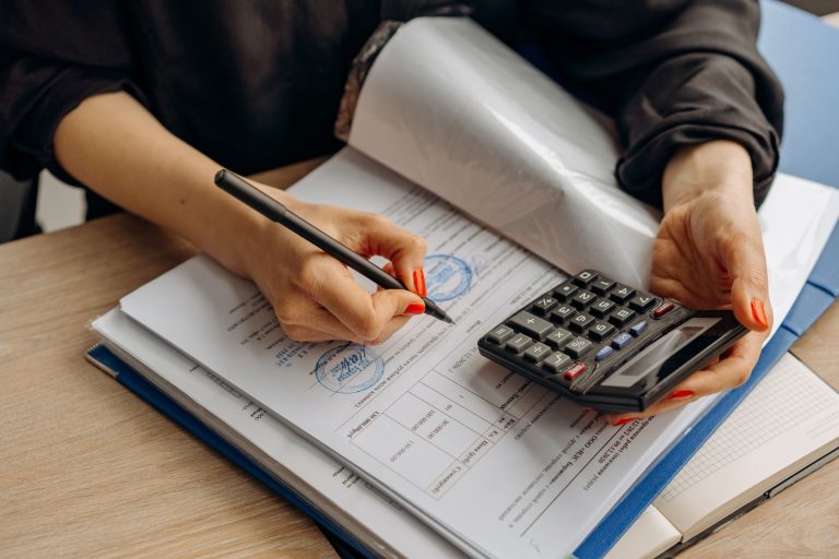 Profissional calcula valores e assina documentos financeiros em uma mesa de escritório.