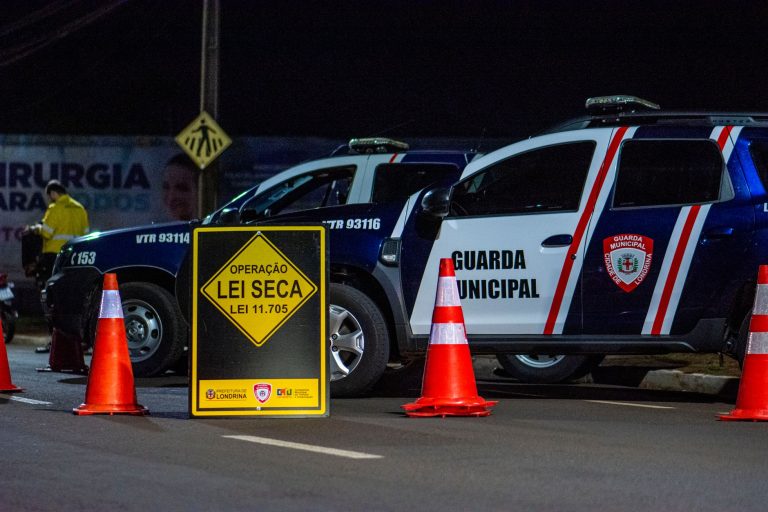 Veículos da Guarda Municipal e cones em um bloqueio de fiscalização noturno em uma via urbana.