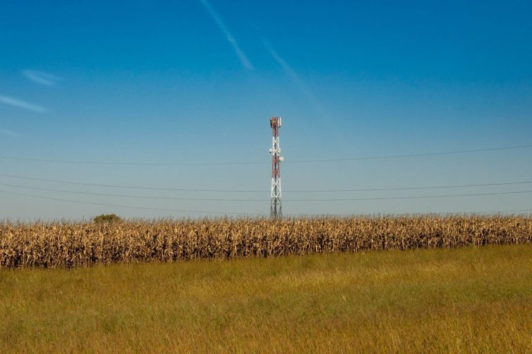 Torre de comunicação instalada em um campo rural sob céu azul.